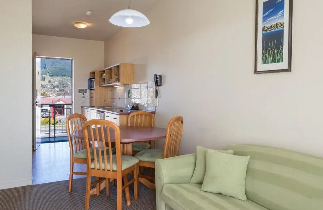 Un espace de vie compact comprenant un coin repas, une kitchenette et un canapé vert.
