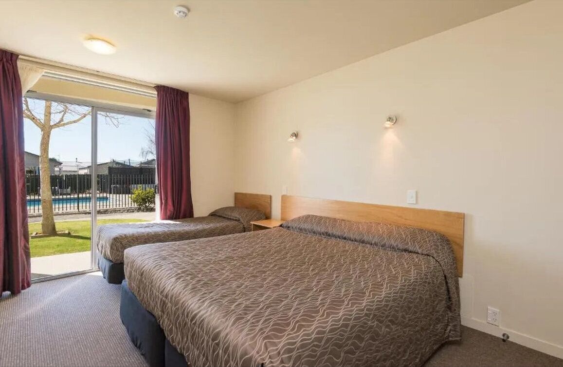 A hotel room with two beds, a large window with curtains, and a view of a pool.