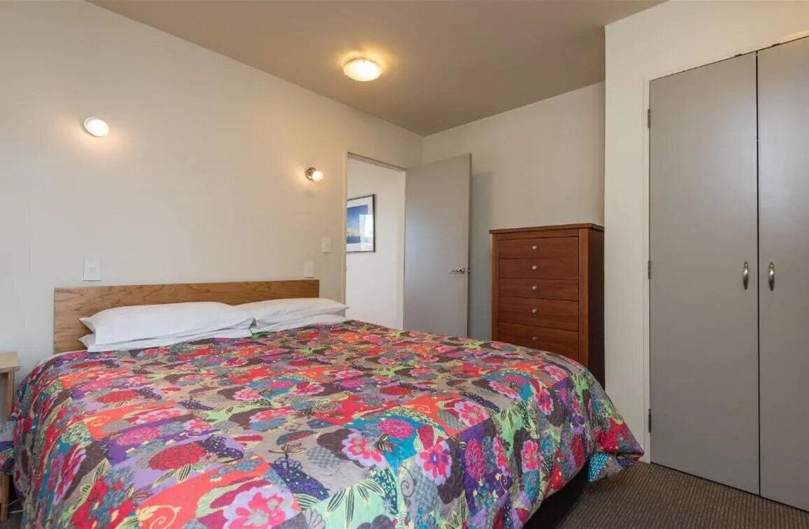Un dormitorio con cama, cómoda de madera, armario y luz en el techo.