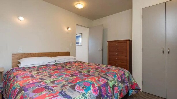 Un dormitorio con cama, cómoda de madera, armario y luz en el techo.
