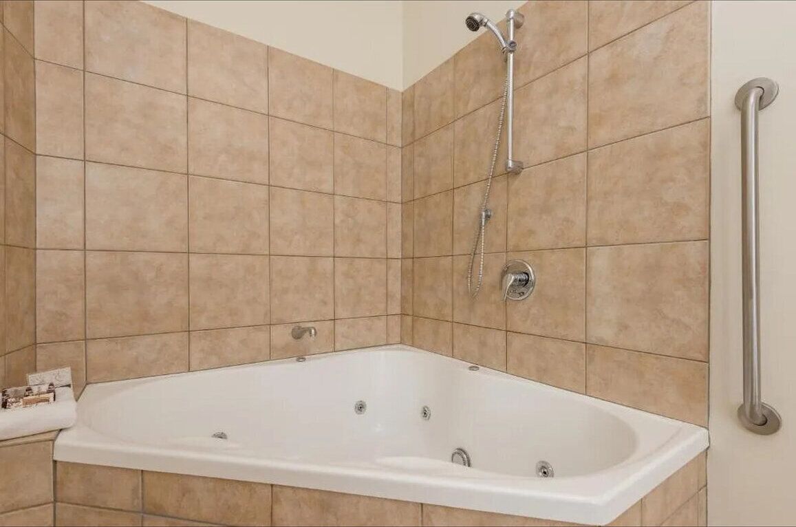 A bathroom with a white bathtub, a showerhead, and a handrail.