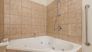 A bathroom with a white bathtub, a showerhead, and a handrail.