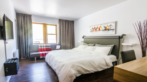 Una habitación de hotel moderna con una cama grande, un escritorio de madera, un televisor de pantalla plana y una ventana con cortinas.