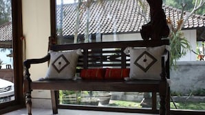 A wooden bench with patterned cushions in a room with a tiled floor and a view of a tiled roof outside. - Baruna Cottages (Kintamani)