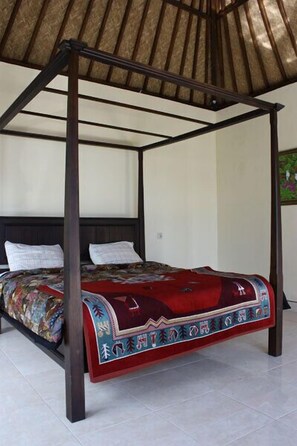 Una cama con dosel con un edredón estampado en rojo y azul, un cabecero de madera y un techo con techo de paja.