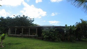 A house with a large glass window, surrounded by lush greenery and a clear sky. - Hostal Pukao (Hanga Roa)