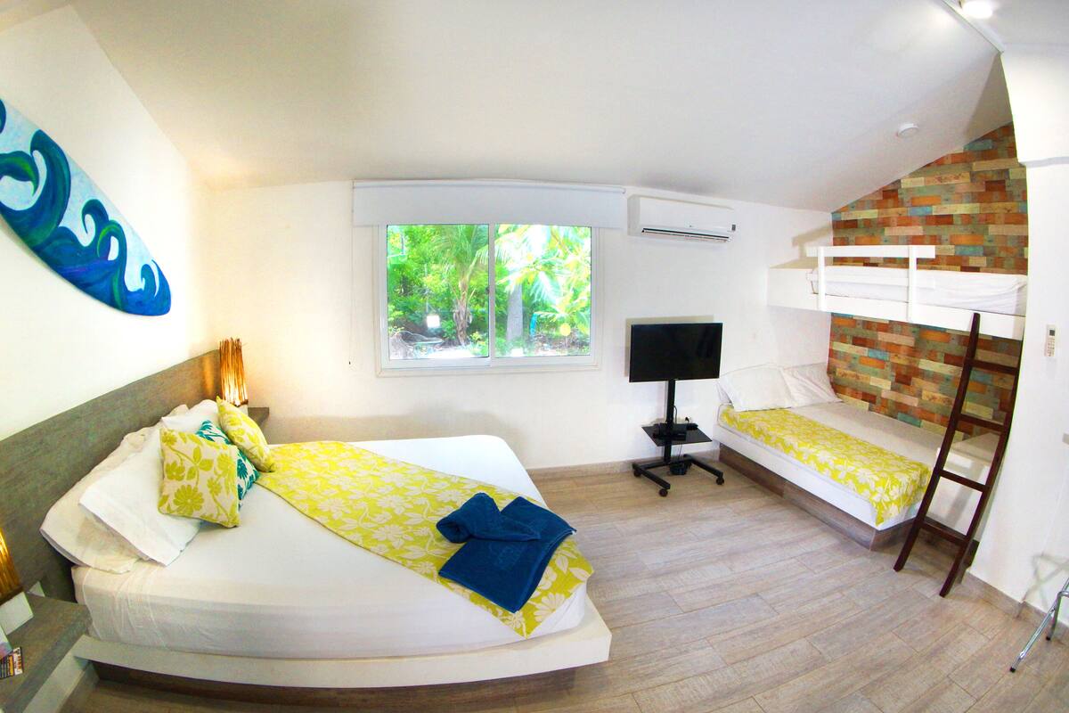 Une chambre avec un lit, un bureau, une télévision, une fenêtre et un lit superposé.