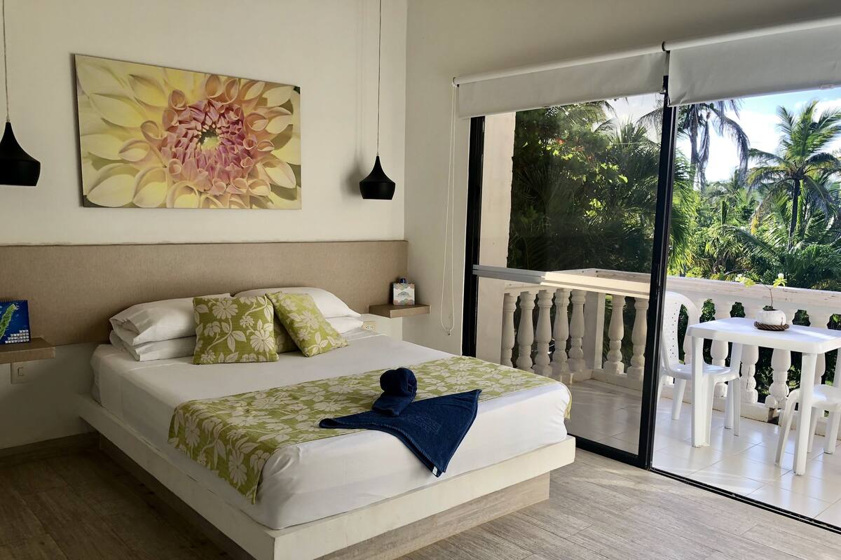 Une chambre à coucher comprenant un lit, un tableau, une table de chevet, une fenêtre et un balcon avec une table et des chaises.