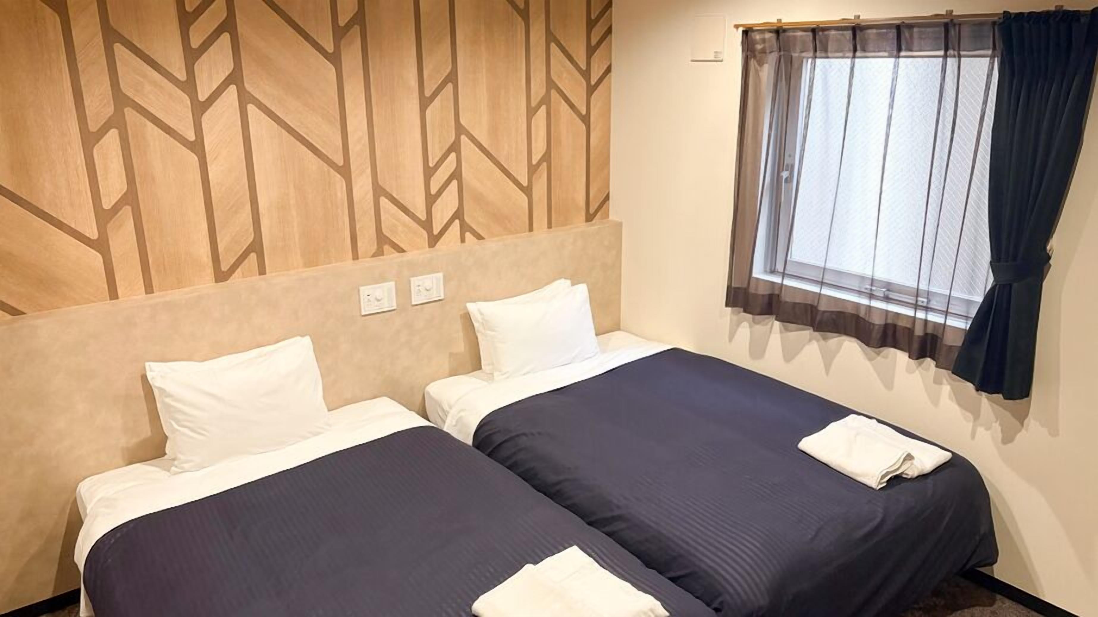 Une chambre d’hôtel avec deux lits, une fenêtre avec des rideaux et un motif géométrique sur le mur.