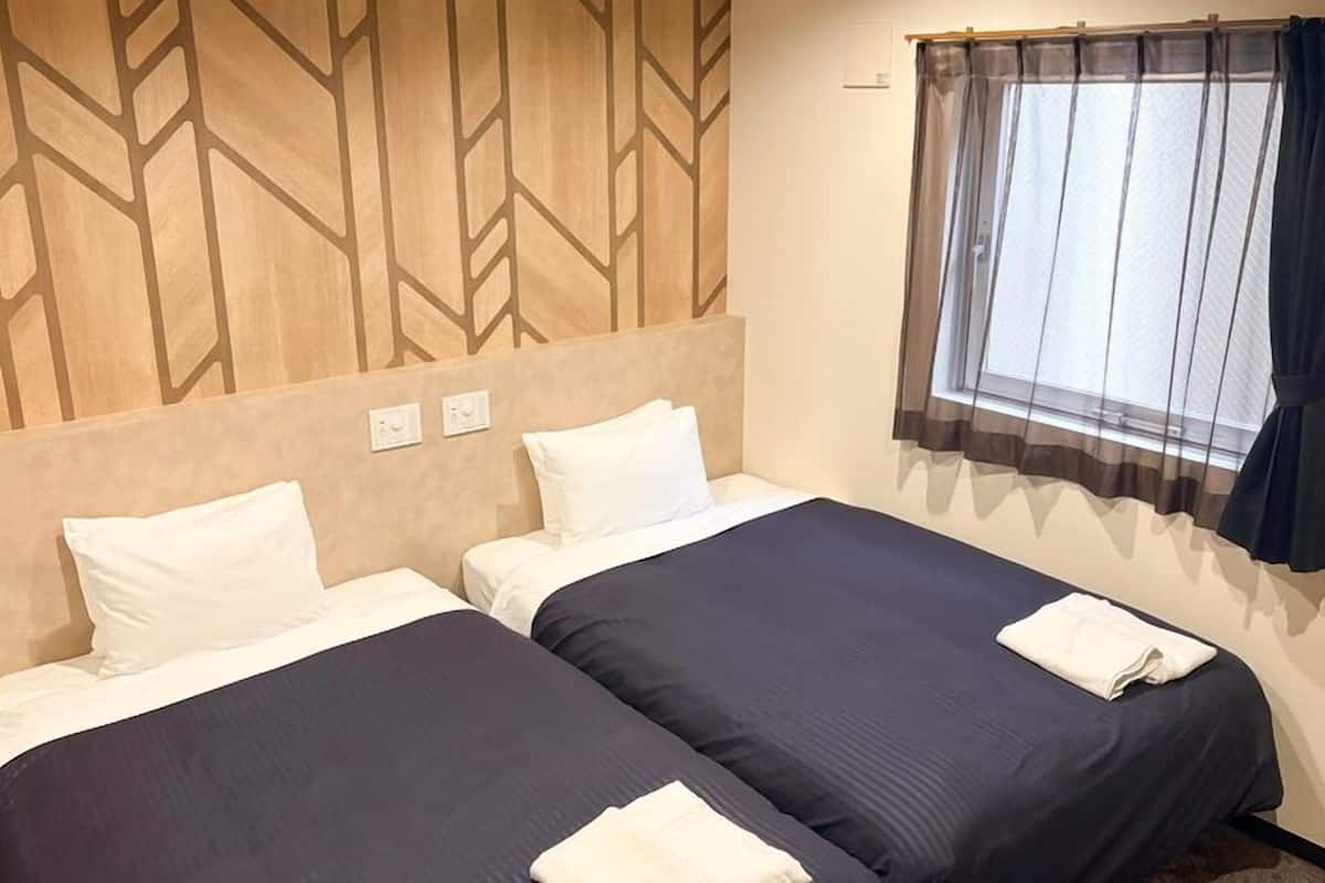 Une chambre d’hôtel avec deux lits, une fenêtre avec des rideaux et un motif géométrique sur le mur.