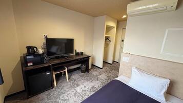 A hotel room with a bed, a desk with a television, a microwave, and a small refrigerator.