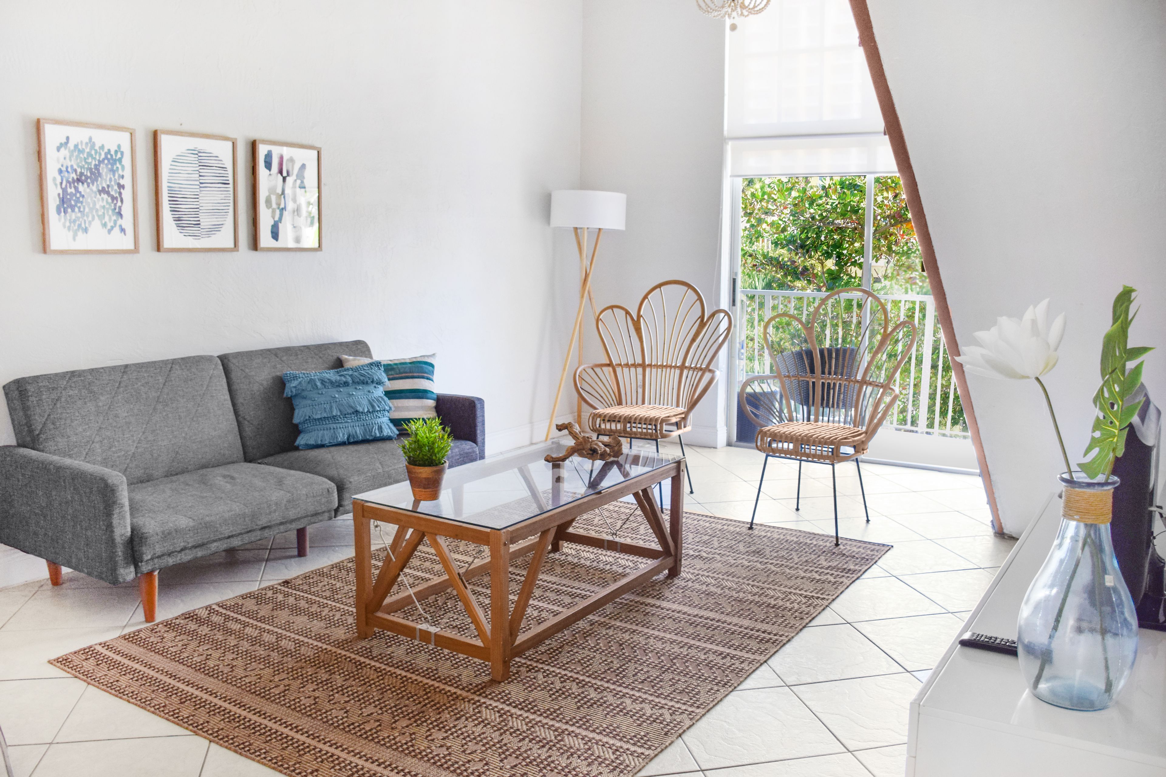 A living room with a grey sofa, a glass coffee table, wicker chairs, and a potted plant.