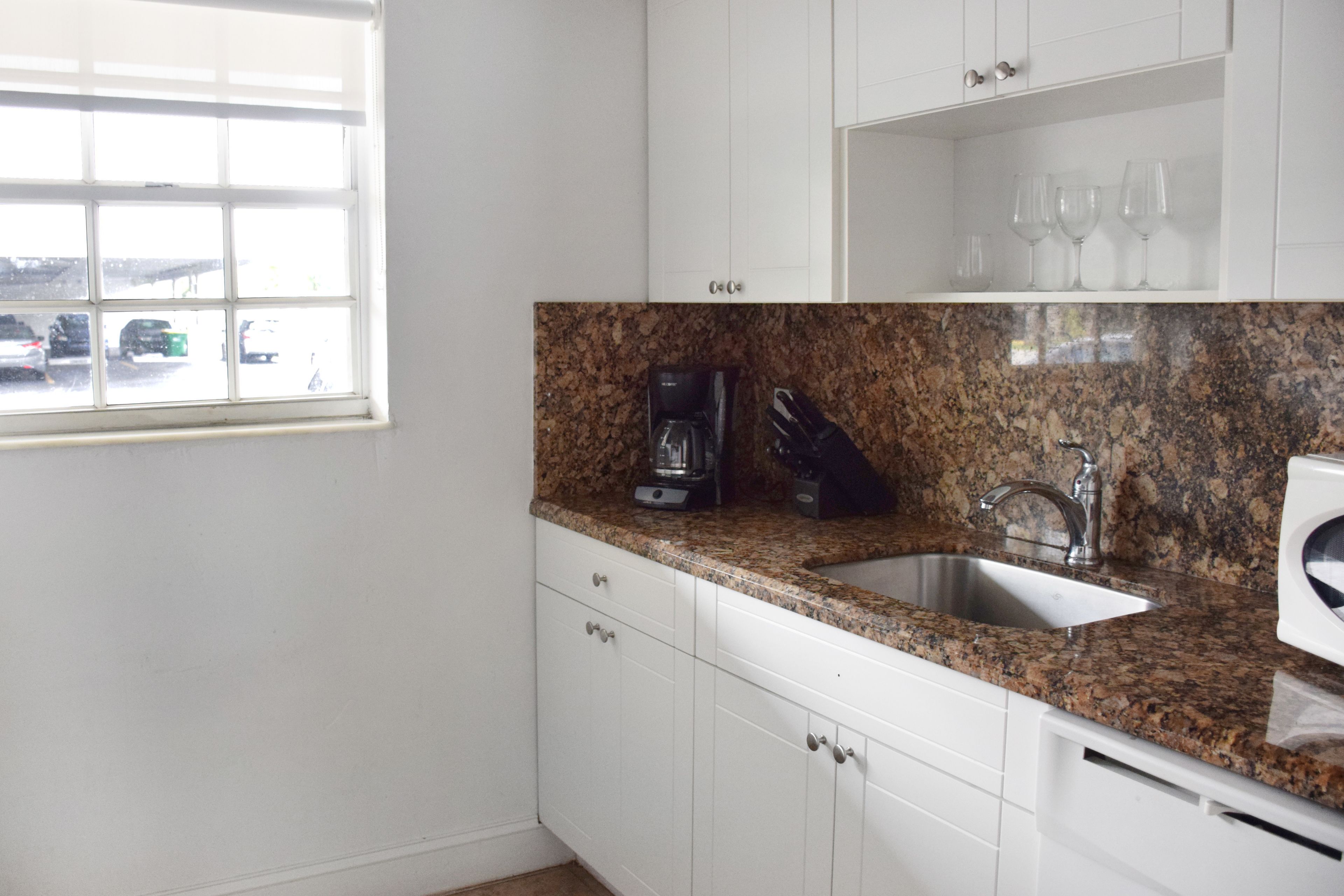 A kitchen with white cabinets, a granite countertop, a coffee maker, and a sink.