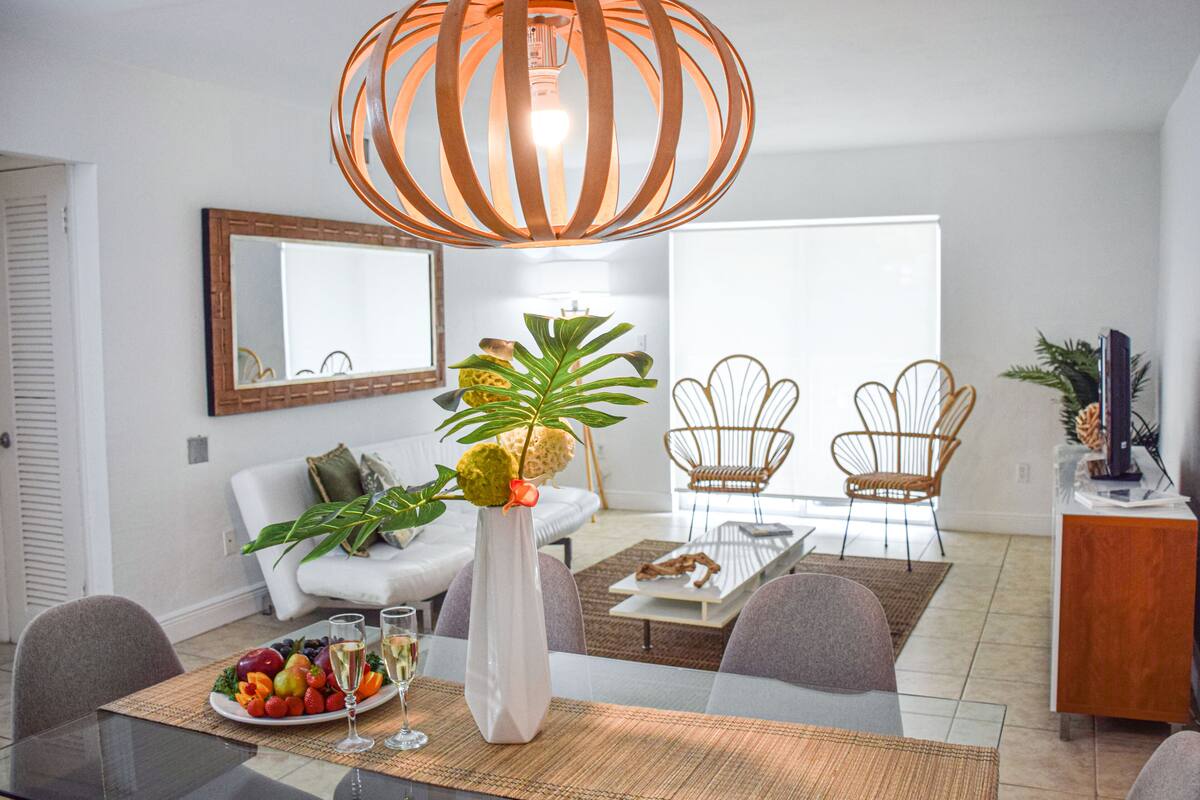 A modern living room with a dining area, white furniture, a large mirror, and a unique pendant light.