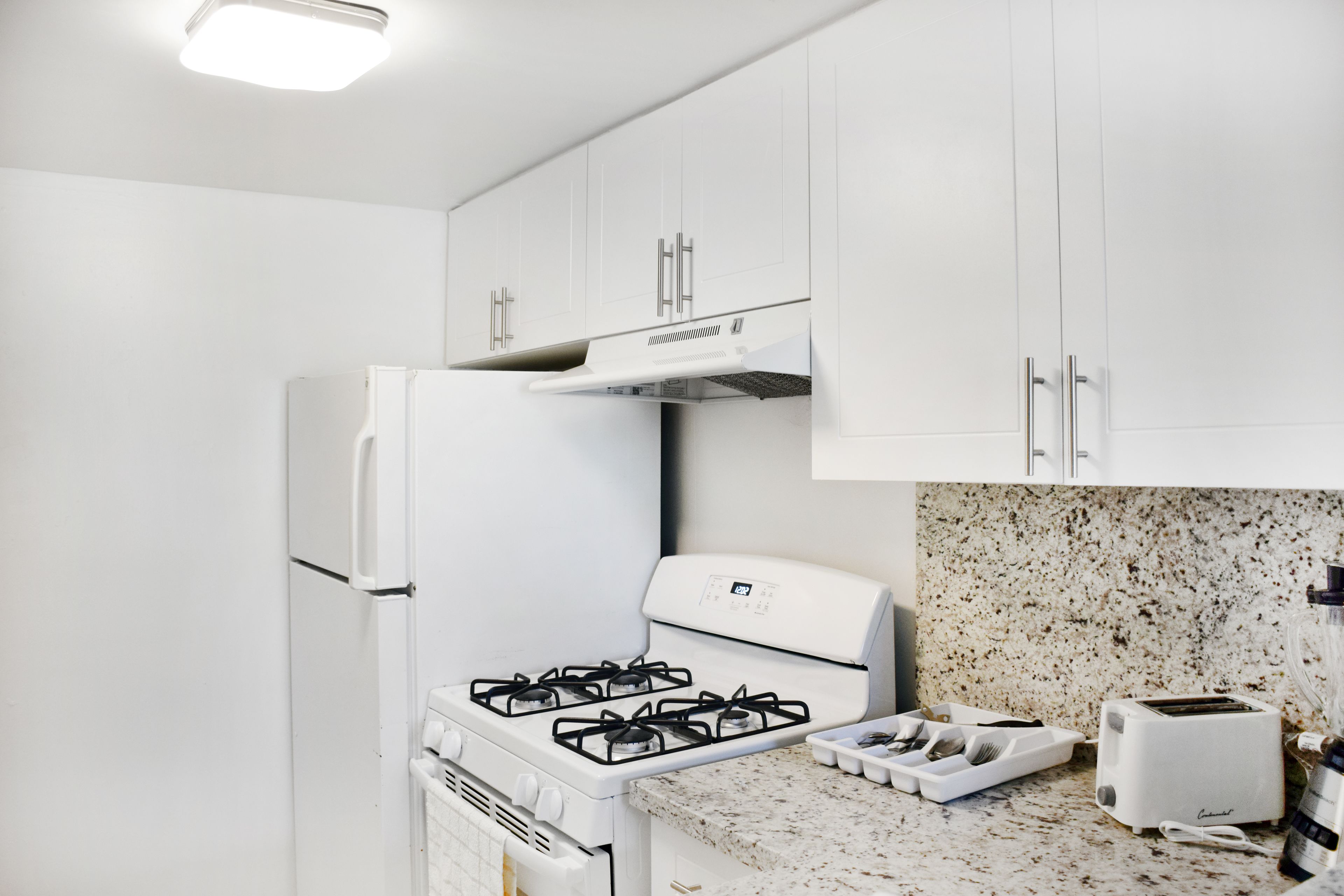 A kitchen with white cabinets, a gas stove, a built-in oven, a microwave, a toaster, and a granite countertop.