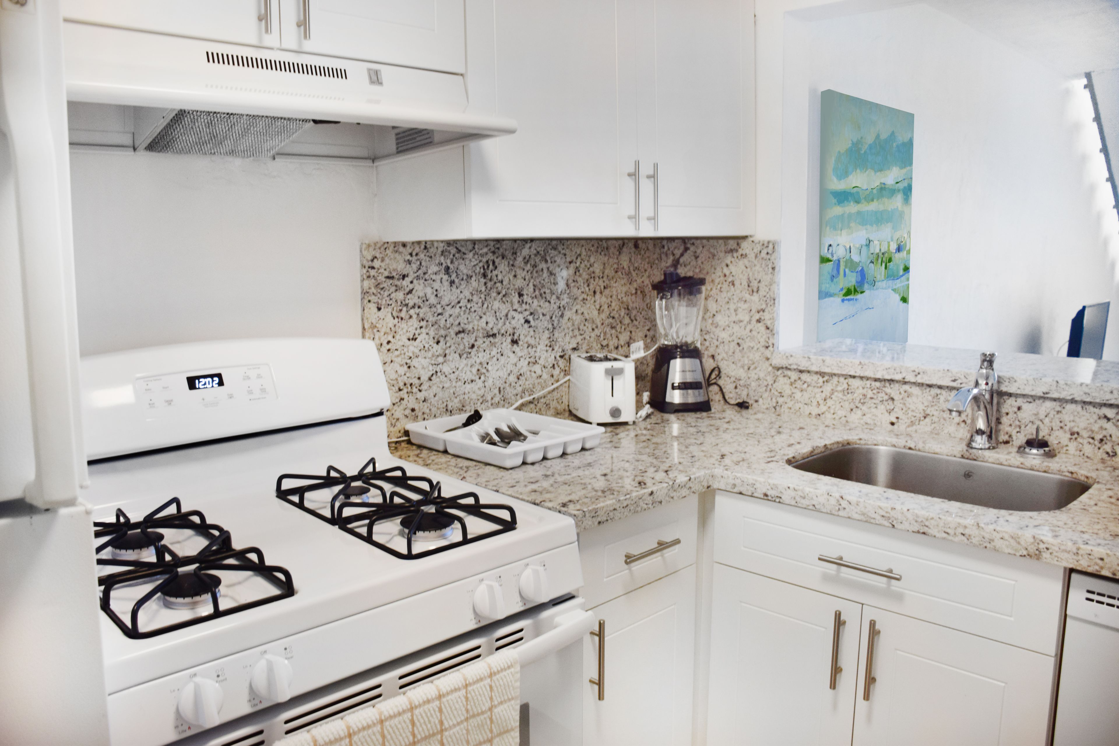 A modern kitchen with white cabinets, a granite countertop, a gas stove, a coffee maker, and a sink.