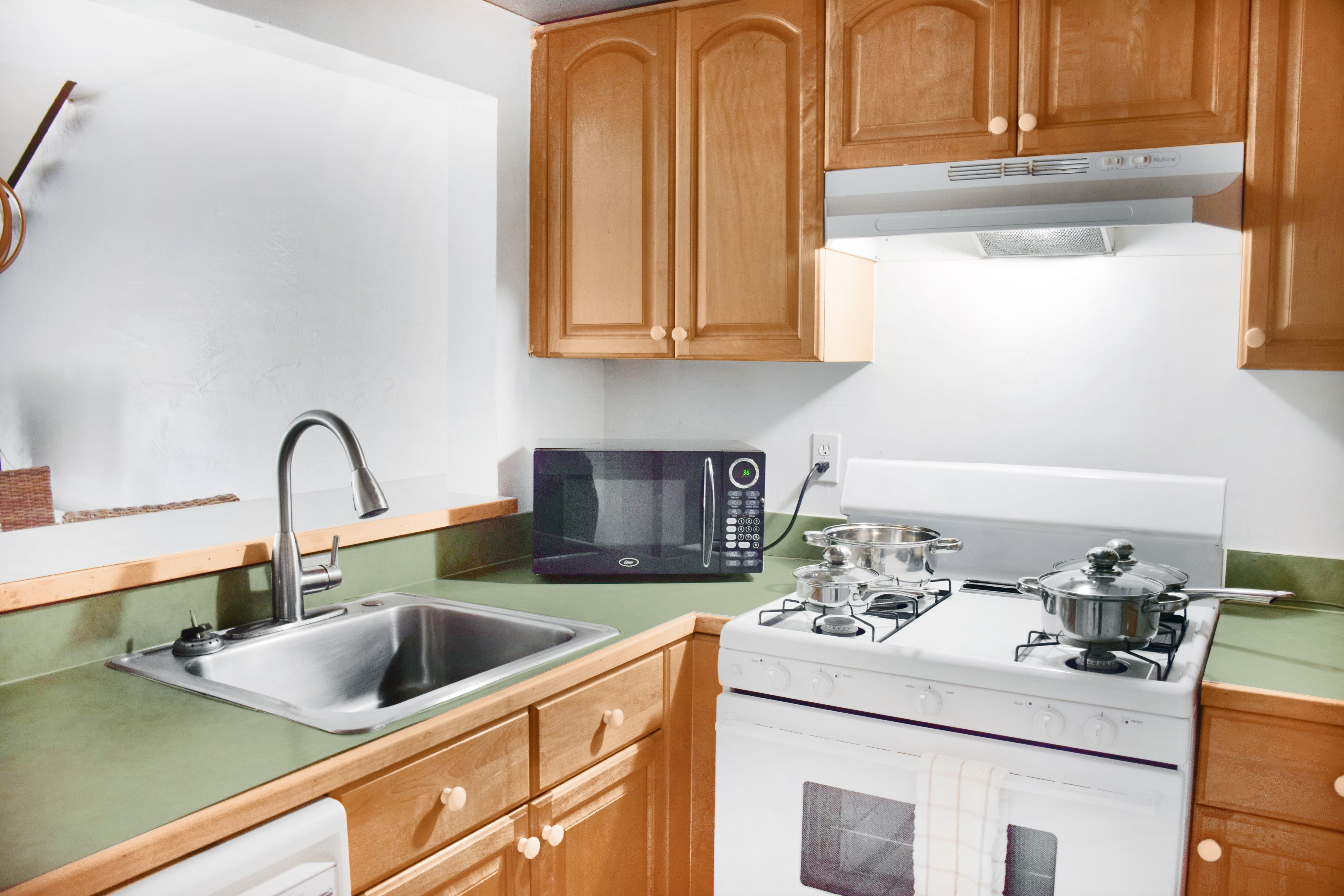 A kitchen with wooden cabinets, a stainless steel sink, a microwave, a stove, and a dishwasher.