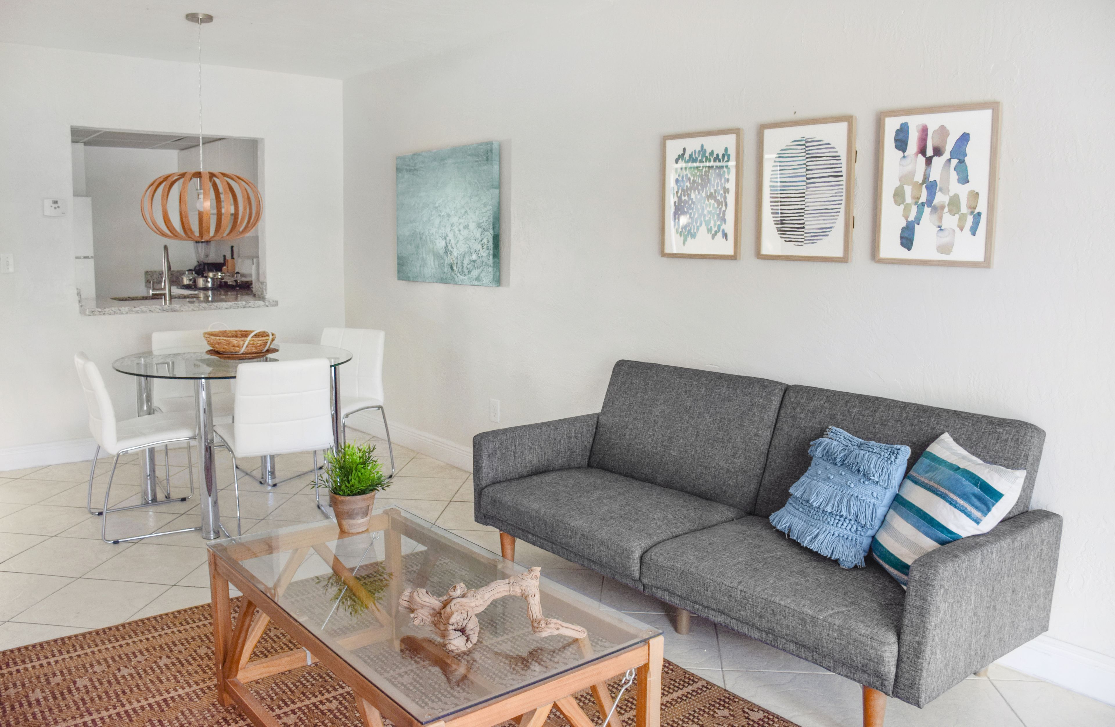 A modern living room with a grey sofa, a glass coffee table, and a dining area with a glass table and chairs.