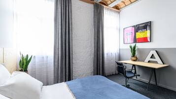 Hotelkamer met een bed, een bureau met stoel, een potplant en twee ingelijste shirts aan de muur.