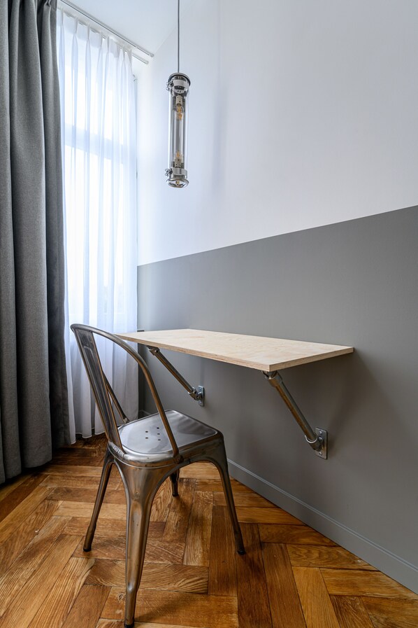 Una esquina de una habitación con piso de madera, una silla de metal, un estante de madera y un colgador de techo.