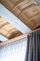 A ceiling with a textured pattern, a window with white curtains, and a wooden beam.