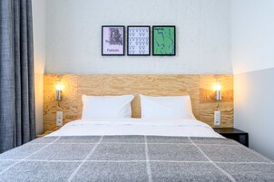 Una cama bien hecha con una colcha a cuadros, dos lámparas de pared y tres cuadros en la pared.