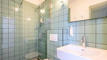 Un bagno con cabina doccia in vetro, un lavandino bianco e uno specchio sopra.
