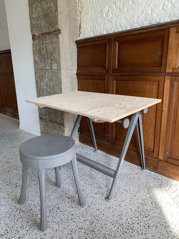 A small wooden table with a grey stool in a room with a concrete wall and wooden paneling. - Hotel La Grande Cloche (Brussels)