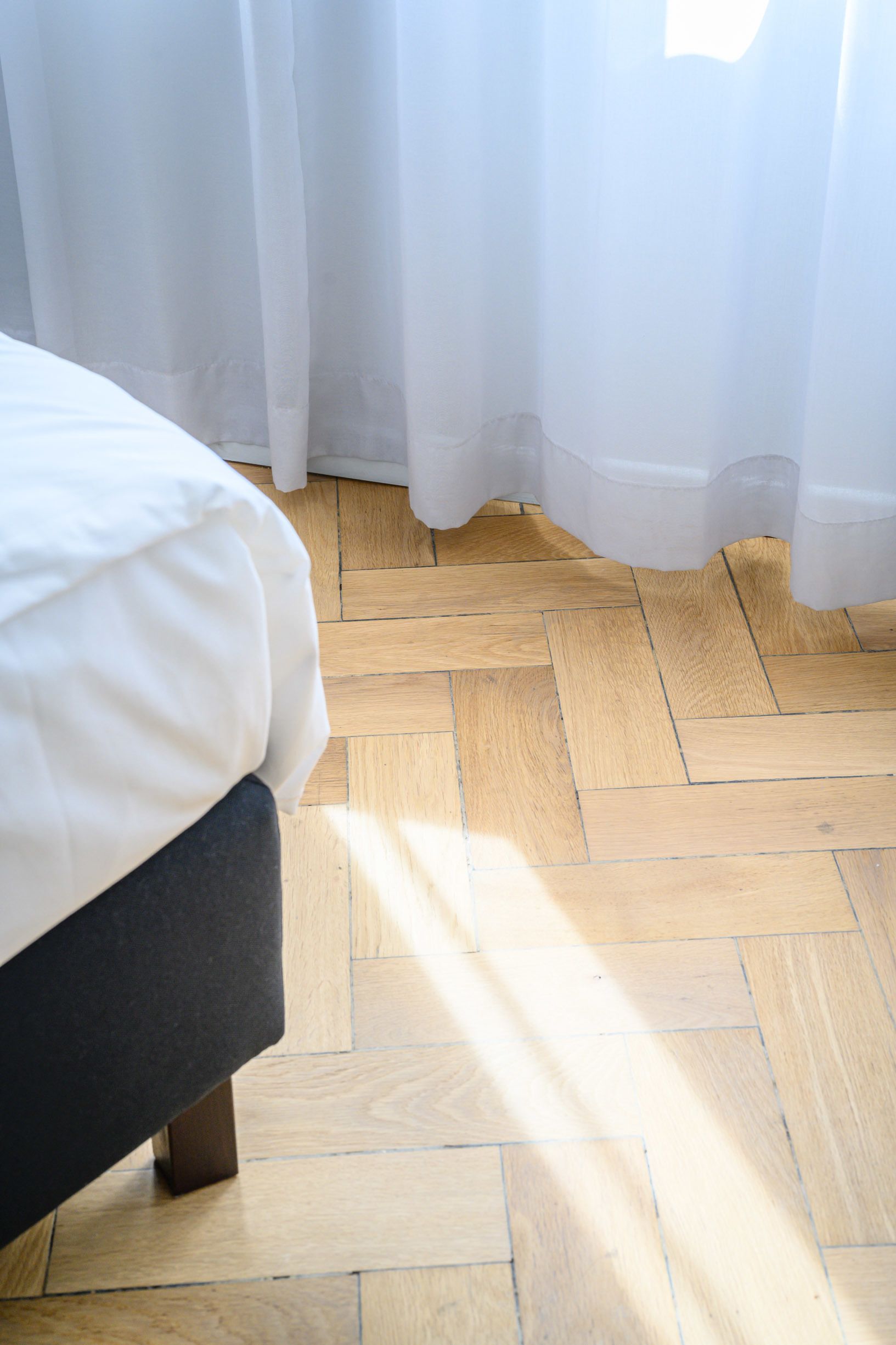 Una cama con edredón blanco, un banco de color oscuro y suelo de parqué de madera.