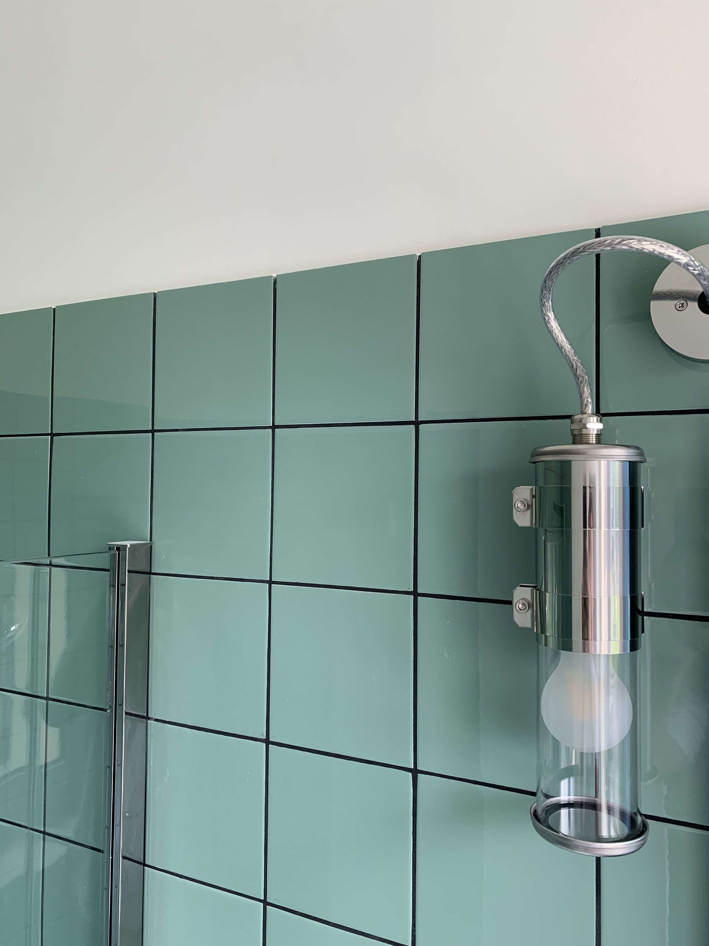A bathroom with teal tiles, a glass shower enclosure, and a metallic light fixture.