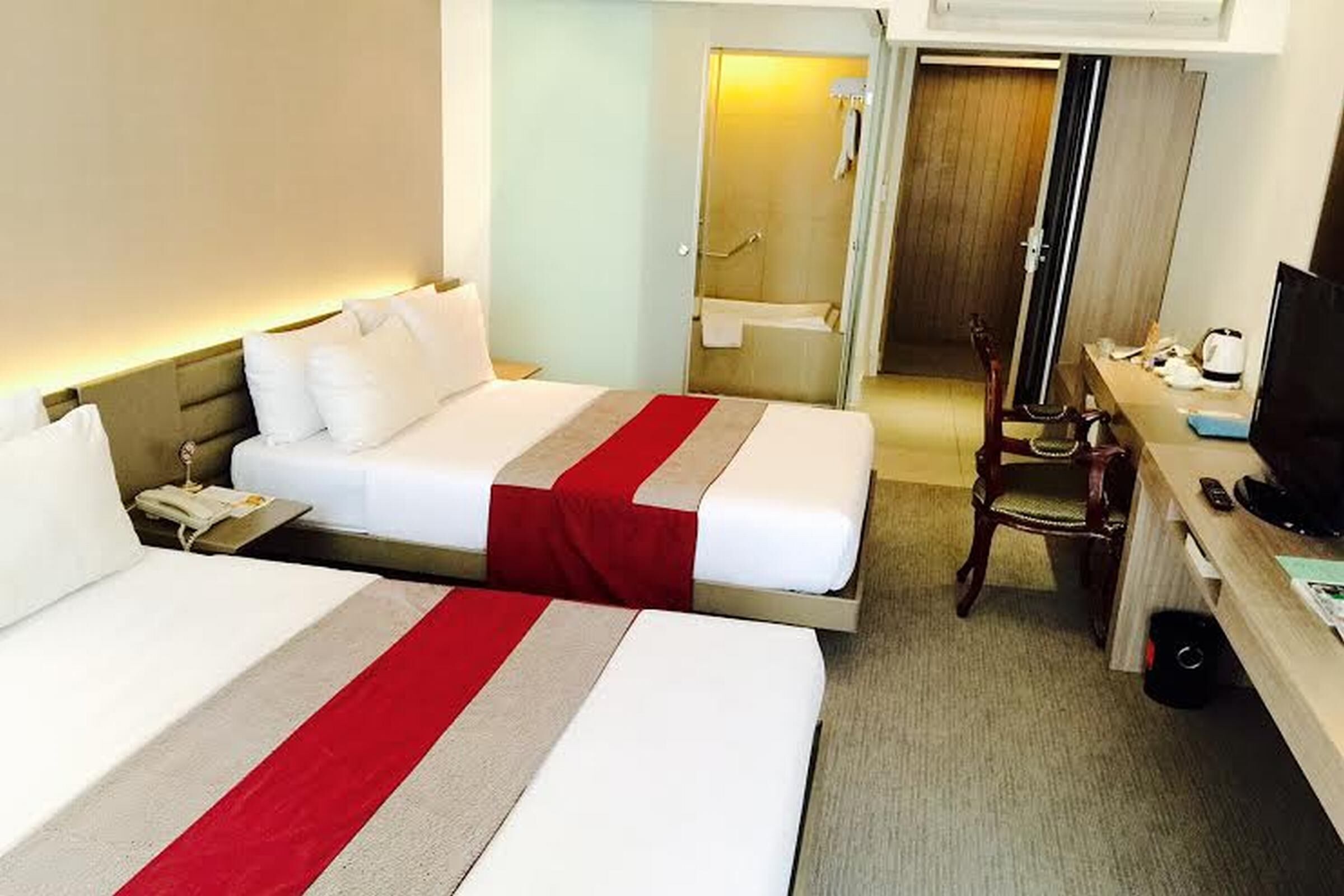 A hotel room with two beds, a desk, a chair, and a television.