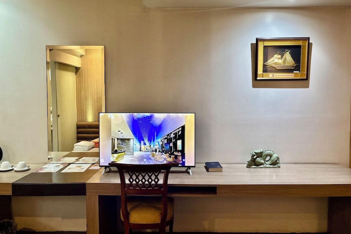 A hotel room with a desk, a television, a framed picture, and a small statue.