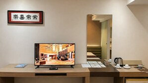 A hotel reception desk with a television displaying a hotel interior, a framed sign, and a coffee station. - The E-Hotel Makati (Makati)