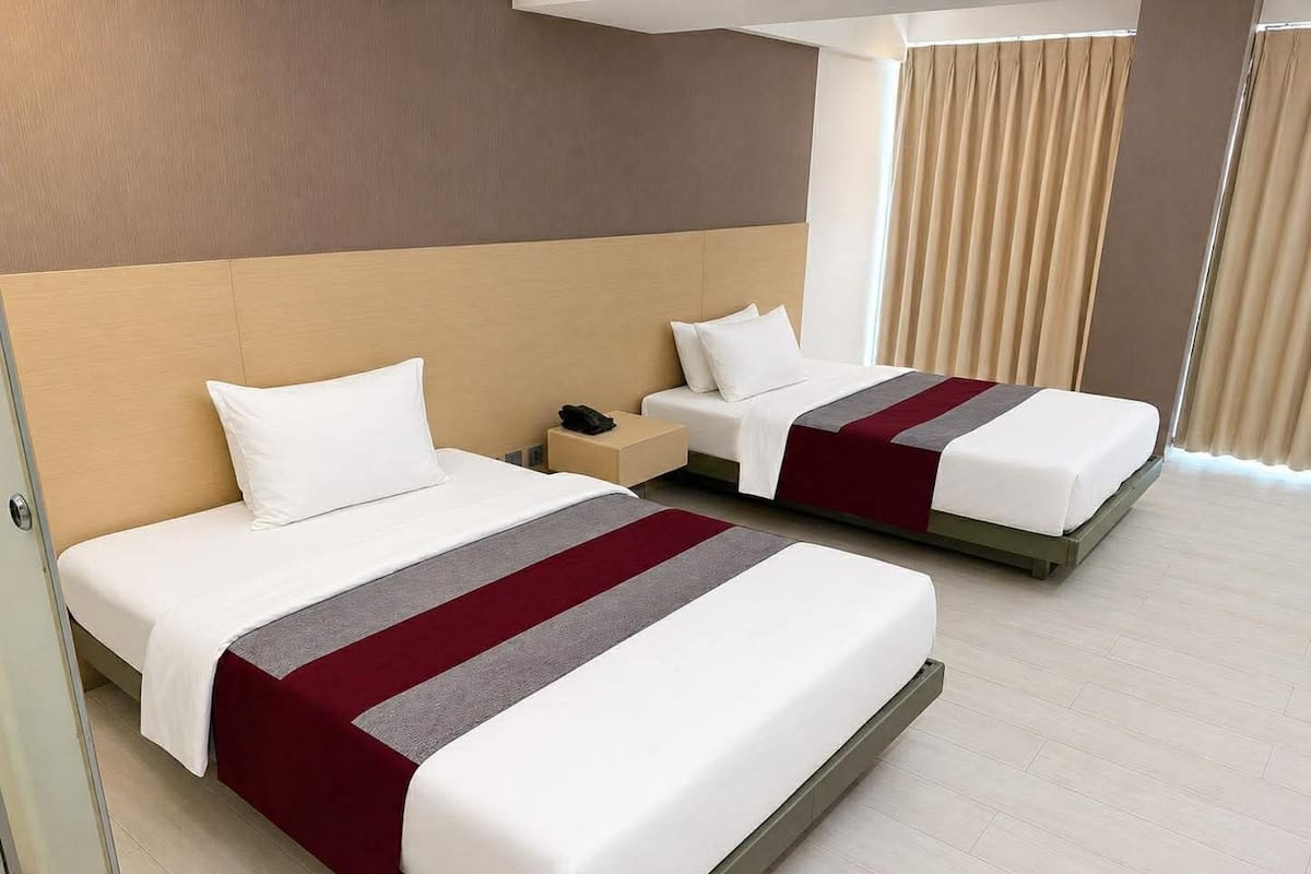 A hotel room with two beds, a bedside table with a phone, and a window with curtains.