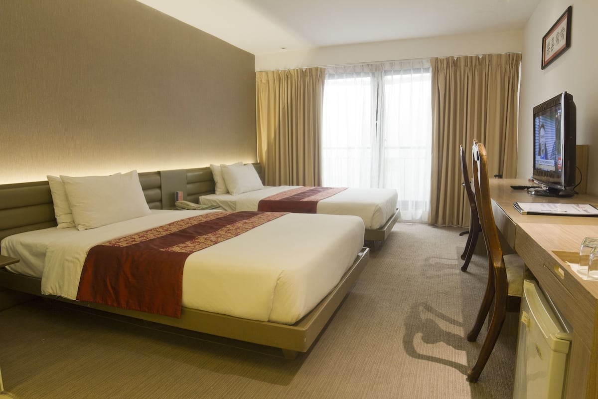 A hotel room with two beds, a desk with a television, and a window with curtains.
