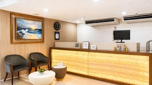 A reception area with a wooden reception desk, two chairs, a clock, a painting, and an air conditioning unit. - The E-Hotel Makati (Makati)