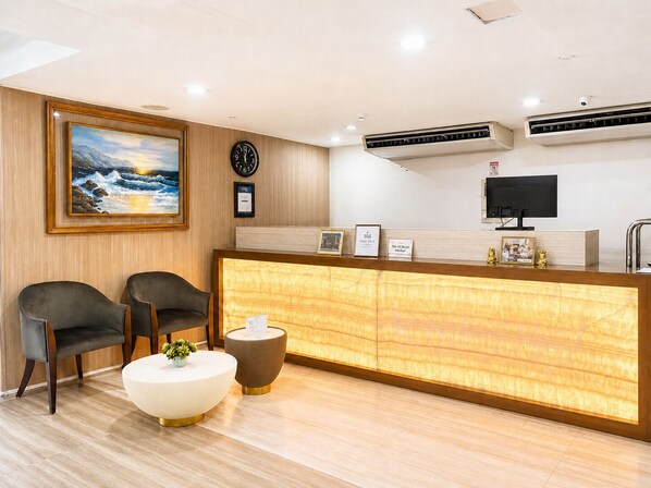 A reception area with a wooden reception desk, two chairs, a clock, a painting, and an air conditioning unit. - The E-Hotel Makati (Makati)