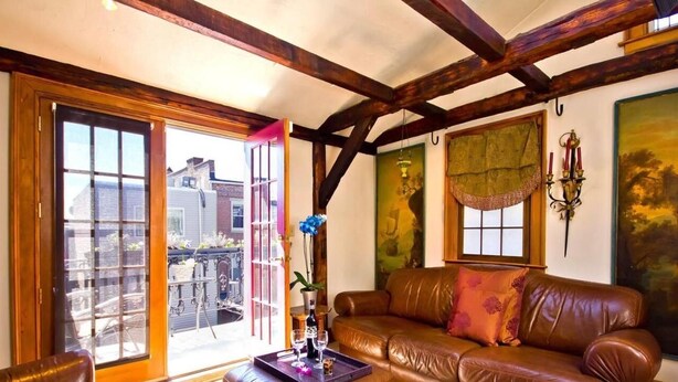 A cozy living room with a brown leather sofa, a matching ottoman, and a glass door leading to a balcony. - Moroccan Boutique Guest House (Boston)