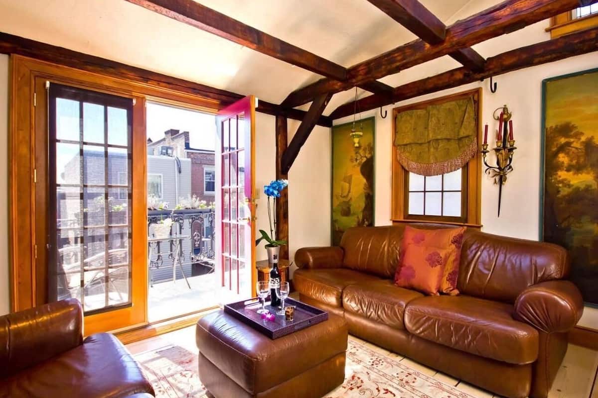 A cozy living room with a brown leather sofa, a matching ottoman, and a glass door leading to a balcony.