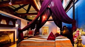 A room with a bed, a hanging canopy, a decorative wall, and a small table with a vase. - Moroccan Boutique Guest House (Boston)