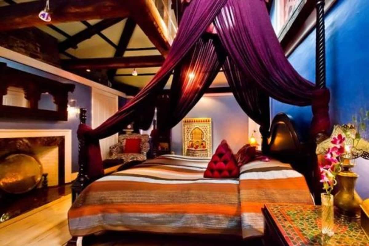 A room with a bed, a hanging canopy, a decorative wall, and a small table with a vase.