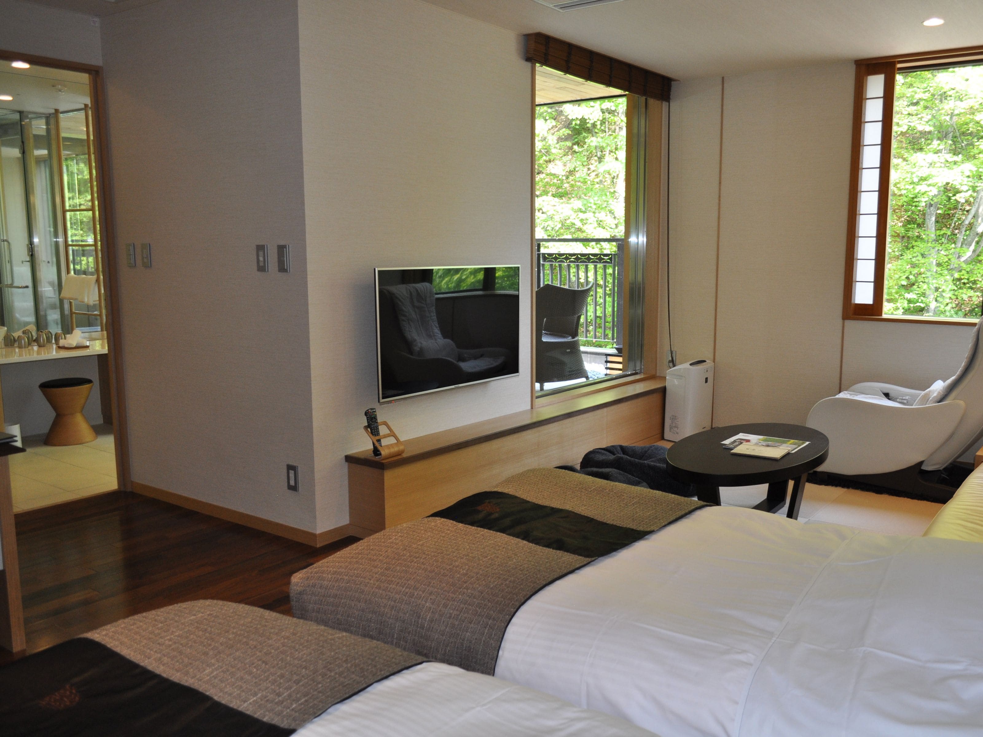 Habitación de hotel moderna con una cama grande, televisión montada en la pared, zona de estar con mesa y ventana con vistas a zonas verdes.