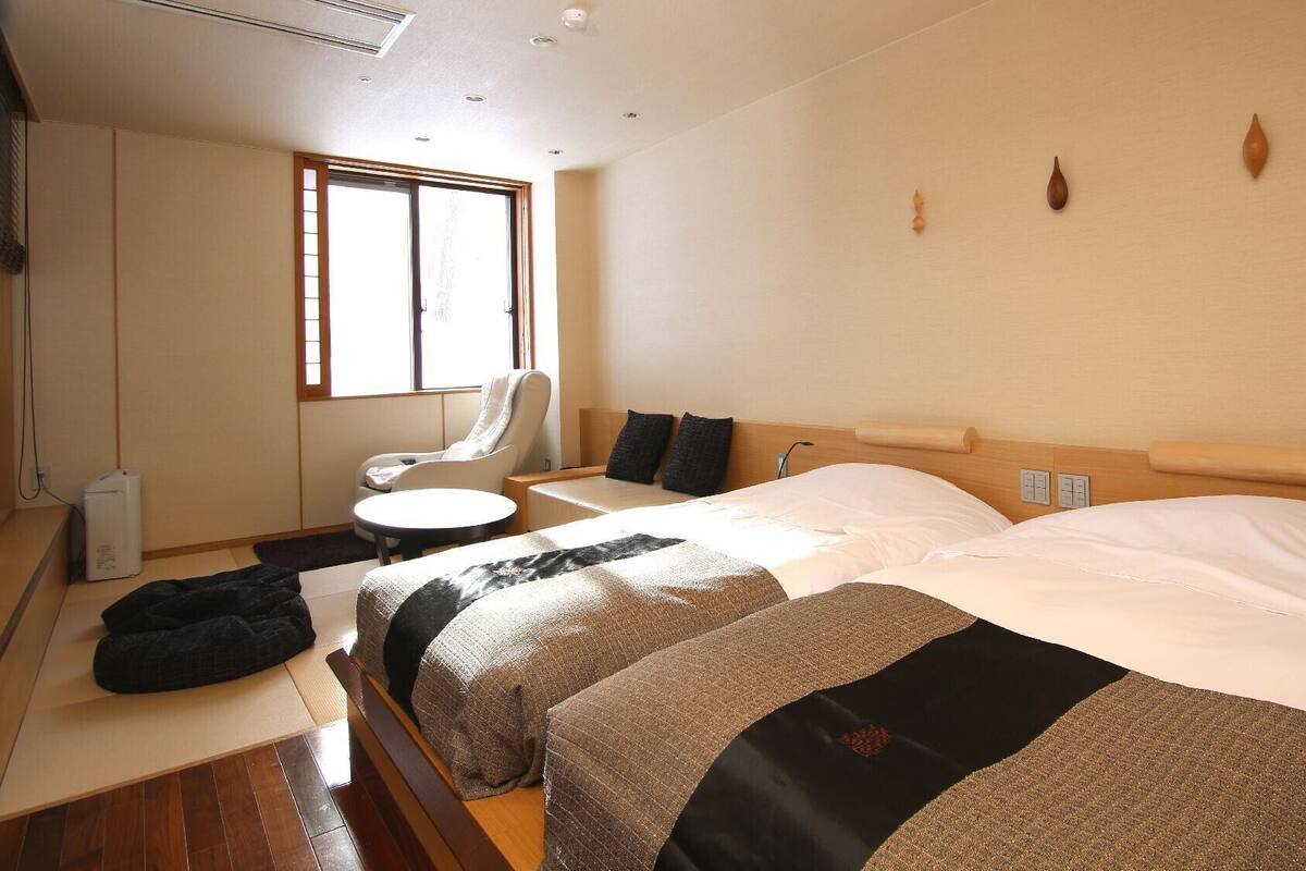 Ein Hotelzimmer mit zwei Betten, einem Sessel, einem kleinen Tisch und einem Fenster.