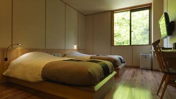 A bedroom with two beds, a desk, a chair, a TV, and a window with a view of trees.