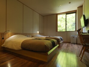 Ein Schlafzimmer mit zwei Betten, einem Schreibtisch, einem Stuhl, einem Fernseher und einem Fenster mit Blick auf Bäume.