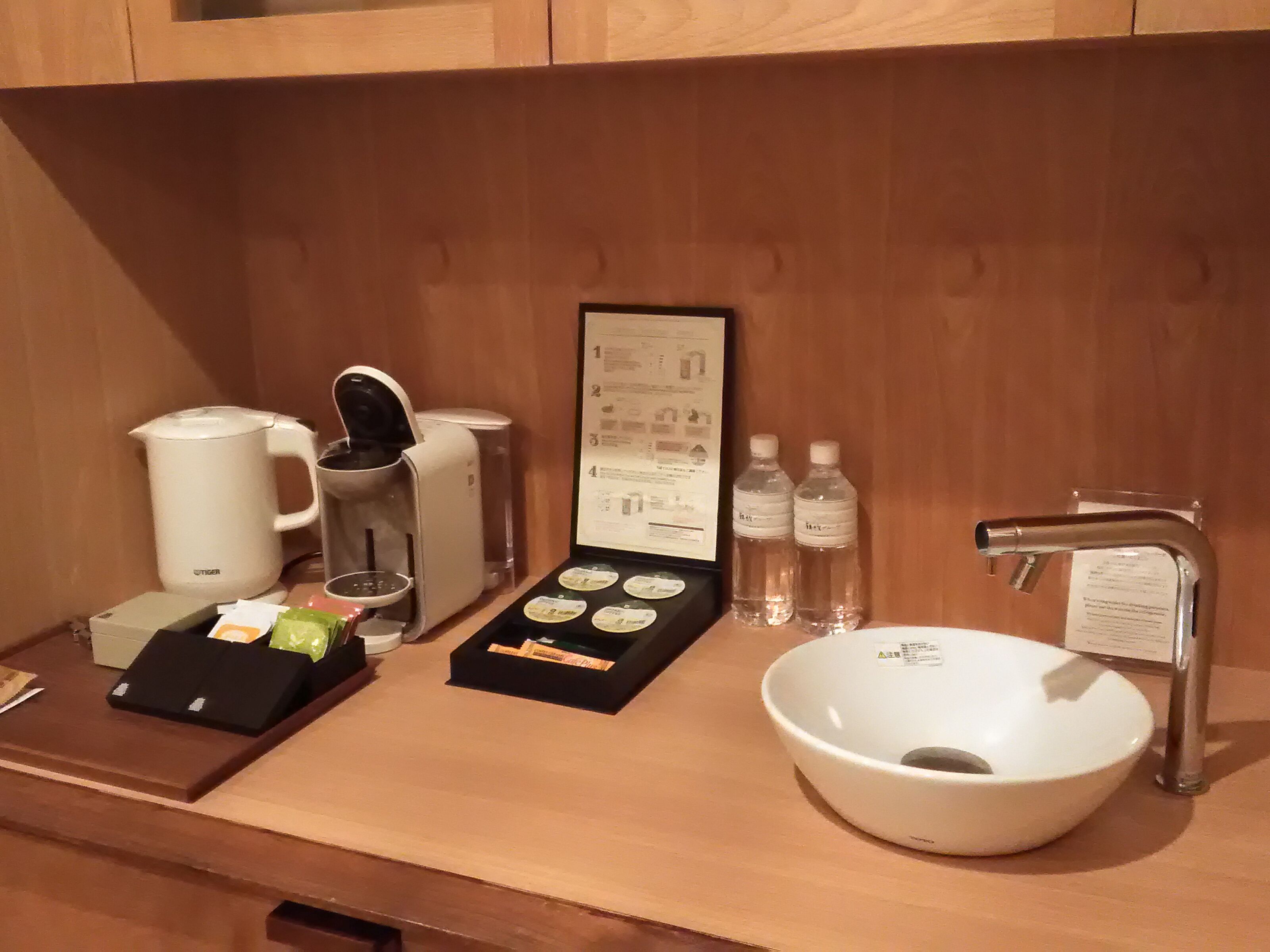 Ein Hotelbad mit Kaffeemaschine, Teezubereiter, Wasserflaschen und einem Waschbecken.