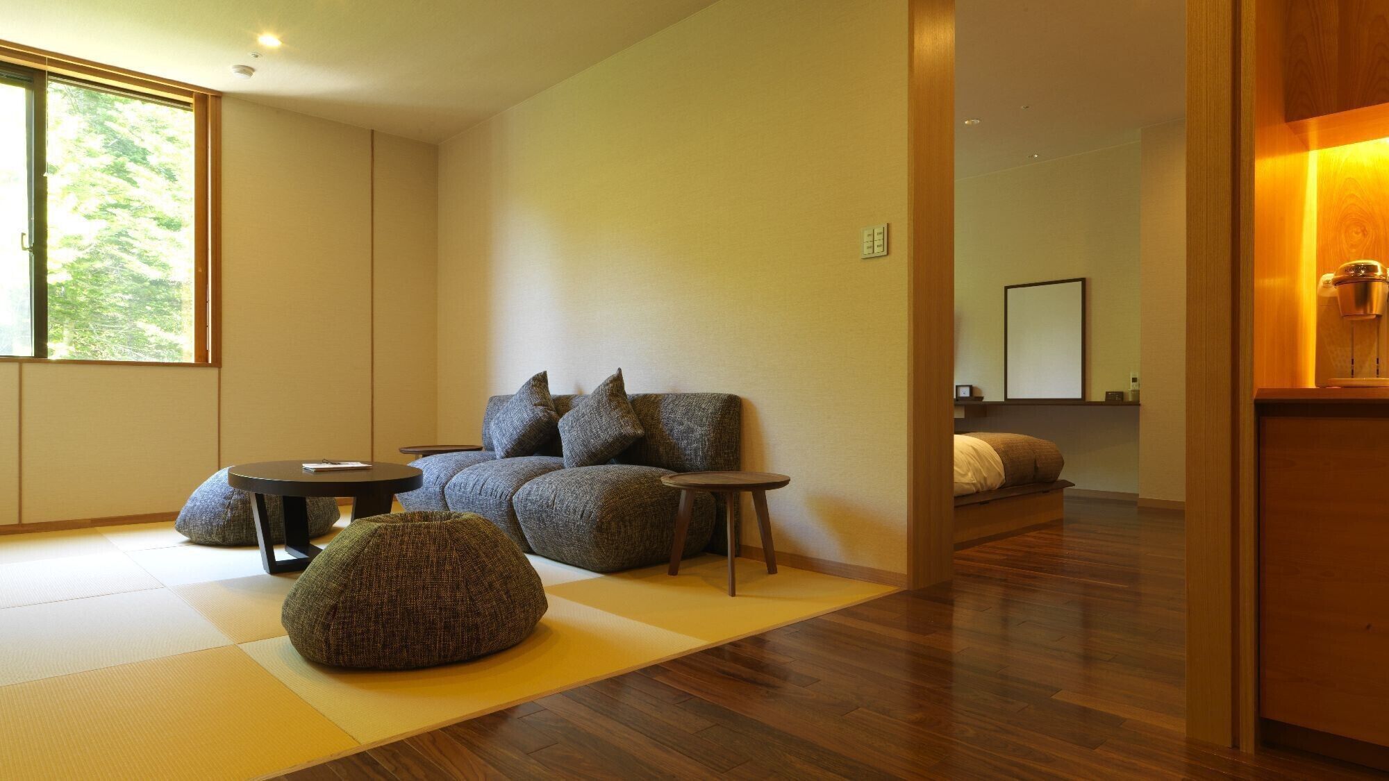 Un salon moderne avec un canapé, deux tables d’appoint, un fauteuil poire, une grande fenêtre et un plancher en bois.