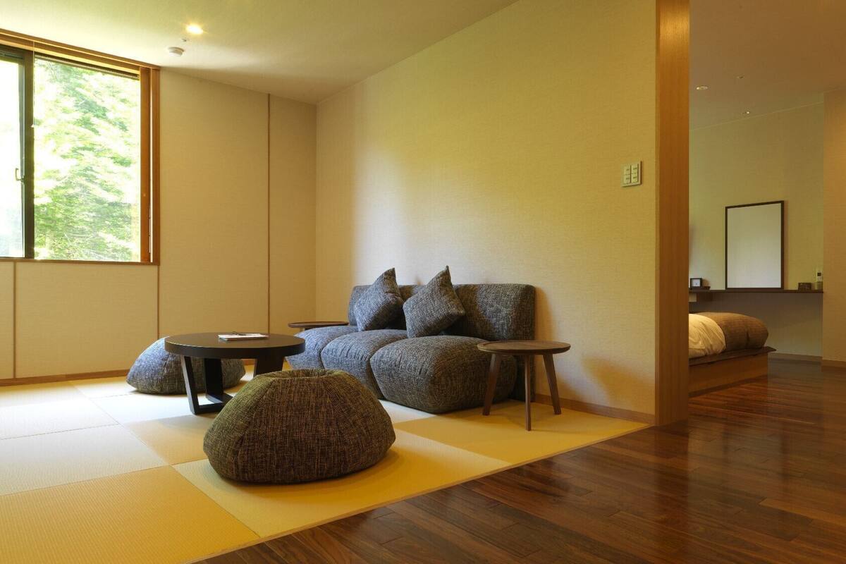Ein modernes Wohnzimmer mit einer Couch, zwei Beistelltischen, einem Sitzsack, einem großen Fenster und Holzboden.