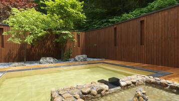 A rectangular hot tub surrounded by a stone border, set against a wooden fence with a tree in the background.