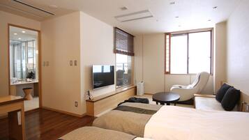 A modern hotel room with a large bed, a seating area, a flat-screen TV, and a window with blinds.